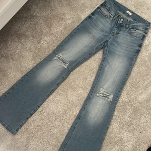 Ljusblå bootcut jeans från Nelly - Snygga ljusblå jeans från Nelly i storlek 36, med bootcut passform och slitna detaljer vid knäna. Jeansen har dubbla knappar i midjan, klassiska fickor bak med knapp och är tillverkade i mjukt denimtyg. Endast använda en gång. 