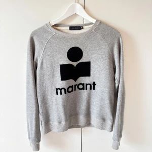 Grå sweatshirt från Isabel Marant - Snygg grå sweatshirt från Isabel Marant med svart logga framtill. Tröjan har rund halsringning, långa ärmar och ribbade muddar vid ärmslut och nederkant. Perfekt för en avslappnad och trendig look. Tröjan är  äkta! Har inget kvitto då det var en present