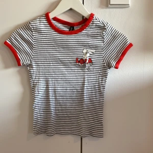 Randig Lola Bunny T-shirt  - Superfin t-shirt med svarta och vita ränder, röd kant vid hals och ärmslut med Lola Bunny-tryck på bröstet. ❤️🤍🖤