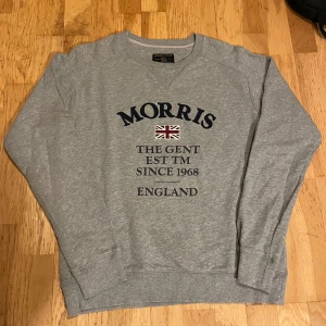 Grå tröja från Morris - Grå sweatshirt i storlek Small från Morris med en broderad brittisk-flagga och text på bröstet. Tröjan är i 100% bomull, har rund hals och långa ärmar. Den har även ribbade muddar vid ärmslut och nederkant. Perfekt för dig som gillar brittisk preppy stil.     Skicka ett DM om du har några frågor!                                          KOLLA MINA ANDRA MORRIS ANNONSER!!