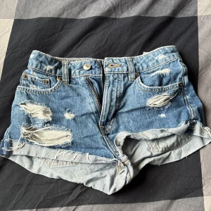 Blå slitna jeansshorts med upprullad kant - Snygga blå jeansshorts med slitna detaljer och uprullad kant