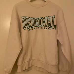 Vit sweatshirt från Gina Tricot - Vit sweatshirt från Gina Tricot i storlek XS med grön text 'ORIGINAL' framtill. Tröjan har rund halsringning, långa ärmar och ribbade muddar.