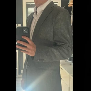 Grå kavaj i Loro Piana Dream Tweed - Tja! Säljer denna gråmelerade kavaj i Loro Pianas Dream Tweed av 100% extrafin ull. Kavajen som är i strl 46 är tillverkad av J.Lindeberg och har en klassisk design med två knappar framtill. Perfekt för en stilren look. Hör av dig om du har några frågor eller funderingar!