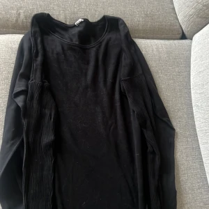 Svart ribbad stickad tröja - Svart stickad tröja med rund halsringning och långa ärmar. Ärmarna har en snygg ribbad detalj som ger extra struktur och stil. Perfekt för dig som gillar en enkel men ändå trendig look. Passar till allt och är superenkel att matcha.