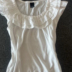Vit söt volangblus - Supersöt vit blus med bred volangkrage och ärmlös design. Från L154 aldrig använd