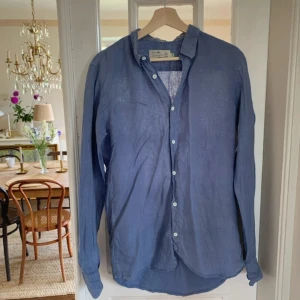 Blå linneskjorta från Directors Cut - Säljer en stilren blå skjorta i linne från Directors Cut. Skjortan har klassisk krage, vita knappar och lång ärm. Perfekt för dig som gillar en avslappnad men ändå snygg look. Luftigt material som passar bra till varmare dagar. Passar M också