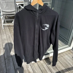 Svart hoodie med dragkedja från GASP - Svart hoodie från GASP i bomull med hel dragkedja, huva och kängurufickor. Tryckt GASP-logga på bröstet och längs ena ärmen i grått. Perfekt för gymmet eller chill. Klassisk passform och långärmad modell. För stor för mig som är 178 cm, 72 kg. Använd en eller två gånger. Kom med prisförslag!!