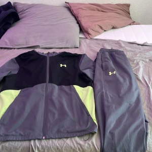 Svart/Grå/grön träningsett från Under Armour - Säljer ett par grå träningsbyxor från Under Armour med resår i midjan och logga i vitt på benet. Perfekta för gymmet eller löprundan. Materialet är syntetiskt och byxorna har en sportig look.