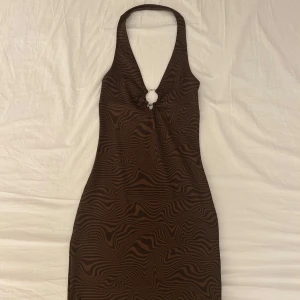 Brun halterneck klänning med zebramönster från H&M - Säljer en brun halterneck klänning från H&M med zebramönster och snygg ringdetalj framtill. Klänningen är kort och har en tight passform som framhäver figuren. I strl xs 