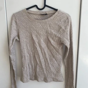 Beige ribbad långärmad tröja från LMTD - Säljer en beige ribbad långärmad tröja från LMTD i storlek S. Tröjan har en rund halsringning och är tillverkad i ett mjukt och stretchigt material som sitter skönt på kroppen. Perfekt basplagg till garderoben.