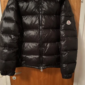 Moncler Maya - Säljer en svart Moncler Maya i bra skick. Inga skador eller defekter, enda är att lite styng på armen har åkt upp men det är inget man själv märker vid användning! Jackan innehåller Scan både på insidan av jackan (bild ovanför) samt på jackärmen. Priset är ej hugget i sten! Alltid öppen för frågor och förhandlingar!