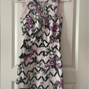Blommig klänning från Guess - Säljer en snygg klänning från Guess med blommigt mönster i lila och grönt. Klänningen har snörning framtill och en figurnära passform. Perfekt för sommarens tillfällen! Aldrig använd.
