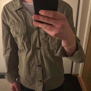 grön overshirt från Morris - Säljer en riktigt snygg olivgrön overshirt från Morris med klassisk krage och två bröstfickor med knappar. Väldigt sällan använd, så riktigt bra skick.