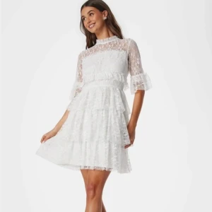 Vit spetsklänning med volanger - Superfin vit kortklänning i spets med volanger. Klänningen har trekvartsärm och den är gjord i fin spetts. Perfekt för dig som vill ha en fin och trendig klänning till studenten eller skolavslutning! Jag tror storleken är 36-38. Den är endast använd på skolavslutning en gång.