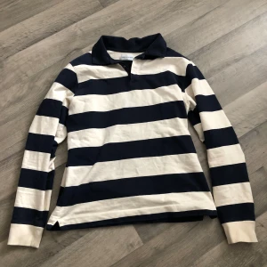 Randig pikétröja från These Glory Days - Säljer en klassisk långärmad pikétröja från These Glory Days i marinblått och vitt. Tröjan har krage och knäppning vid halsen. Storlek S och Orginalpris är 600 kr