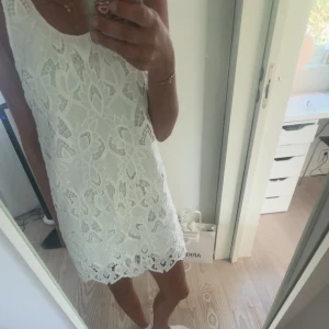 Vit spetsklänning från H&M - Aldrig använd. Säljer en vit ärmlös klänning från H&M med vackra spetsdetaljer och blommigt mönster. Klänningen har rund halsringning och är i kort modell, perfekt för sommarens tillfällen. 