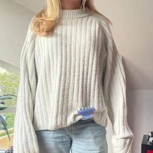 Vit stickad tröja med ribbad struktur - Säljer en vit stickad tröja med ribbad struktur och rund hals. Tröjan har långa, vida ärmar och en avslappnad passform. Perfekt för lager-på-lager och enkel att matcha med jeans eller kjol.
