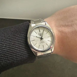 Seiko Quartz Mod - Seiko Quartz med helsilvrig design och stilren vit urtavla. En klocka som passar perfekt både till vardags och vid mer uppklädda tillfällen. Mycket bra skick och ett Quartz urverk.