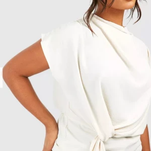 Beige blus från Boohoo - Säljer en stilren vit omlottklänning från Boohoo med draperad framsida och knyt i midjan. Klänningen har korta ärmar och en mjuk, lätt struktur i materialet. Perfekt för dig som gillar minimalistisk och modern stil. Använd en gång. Slutsåld storlek 36