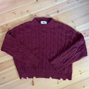 Vinröd kabelstickad tröja från scuffers - Säljer en vinröd kabelstickad tröja med croppad passform och rå kant nertill från scuffers. Tröjan har långa ärmar och rund halsringning. Tröjan är cropped stil så sitter snyggt vid midjan.