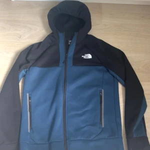 Blå och svart hoodiejacka från The North Face - Säljer en blå och svart hoodiejacka från The North Face med dragkedja framtill och två fickor med dragkedja. Jackan har huva och logga på både bröstet och ryggen. Perfekt för vardagsbruk och enkel att matcha.köpt på jds för 900kr och den är knappt använd.