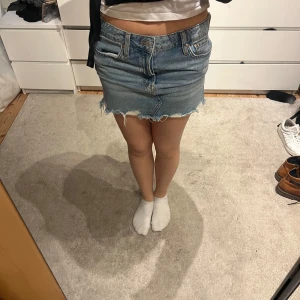 Jeanskjol med fransig kant - Säljer en klassisk blå jeanskjol med rå, fransig nederkant och femficksmodell. Kjolen har normal passform och är i kort längd, låg midjad o kostar från börjar runt 900 kr