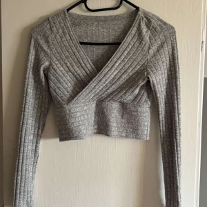 Grå ribbad omlottopp - Säljer en grå croppad omlottopp med lång ärm och ribbad struktur. Storlek XS men känns som S💕