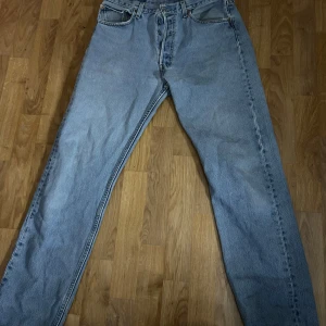 Ljusblå Levis 501 jeans - Klassiska ljusblå Levis 501 jeans med raka ben och knappgylf. Jeansen har fem fickor och tydliga Levis-detaljer som röd etikett på bakfickan och läderpatch bak i midjan. Perfekta för en avslappnad stil.