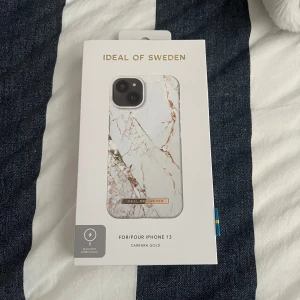 Carrara Gold mobilskal från IDEAL OF SWEDEN - Snyggt mobilskal i marmorlook med guldiga detaljer från IDEAL OF SWEDEN. Passar iPhone 13 och har en vit bas med bruna och guldiga ådror. Skalet är kompatibelt med magnetisk laddning och har en elegant design. Helt nytt och oöppnat
