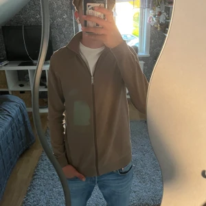 Beige ziptröja med hög krage  - Säljer en beige ziptröja med hög krage och rak passform. Tröjanhar dragkedja framtill och är långärmad. Tröjan är från selected homme 