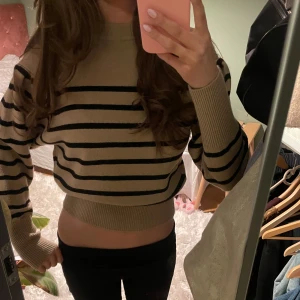 Beige och svart randig stickad tröja  - Säljer en beige stickad tröja med svarta horisontella ränder. Tröjan är någorlunda croppad och har långa ärmar samt ribbade muddar vid ärmslut och nederkant. Tröjan är helt oanvänd, men lappar saknas.
