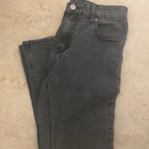 Grå jeansbyxor med rak passform - Säljer ett par klassiska grå jeansbyxor med normalhög midja och raka ben. Byxorna har fyra fickor, knapp och dragkedja framtill. Perfekta för en avslappnad och stilren look. ABS! Pris går att diskutera. (STORLEK 30/32)