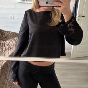 Svart satin topp med spetsdetaljer från Vero Moda - Säljer en svart långärmad topp från Vero Moda. Toppen har bred båturringning och vackra spetsdetaljer vid ärmsluten som ger en elegant touch. Säljer denna jätte fina satintopp från Vero Moda. Den är köpt från Nelly och är endast provad, ej använd. Prislappen finns kvar. Säljer den då den inte kommit till använding💗💗
