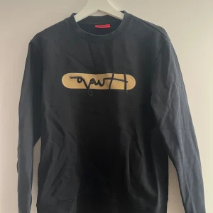 Svart sweatshirt med beige tryck - Svart sweatshirt med rund hals och ett beige tryck framtill. Tröjan har långa ärmar och en avslappnad passform. Perfekt för en stilren och enkel look.