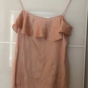 Ljusrosa topp från Zara  - Säljer en ljusrosa topp från Zara med tunna axelband och volangdetalj upptill. Den har en enkel och luftig design, perfekt för varma dagar. Tillverkad i ett mjukt och lätt material.