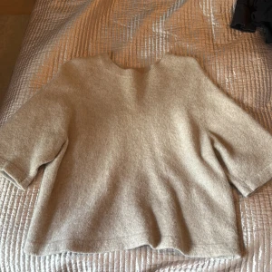 Beige ulltröja från & Other Stories - Mysig beige tröja från & Other Stories, gjord i ullblandning. Tröjan har en rak, lite boxig passform med trekvartsärmar och rund halsringning. Perfekt för lager-på-lager under kyliga dagar.