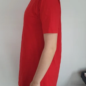 Röd kortklänning i bomull - Enkel och stilren röd kortklänning med rund halsringning och korta ärmar. Klänningen har en rak passform och är tillverkad i mjuk bomull, perfekt för en avslappnad look.