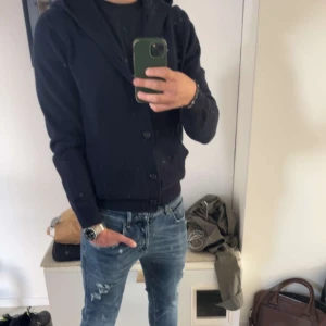 Kofta  - Säljer en mörkblå stickad hoodie från Les Deux med knappar framtill och två fickor. Tröjan har huva och ribbade muddar vid ärmslut och nederkant. Perfekt för kyliga dagar och enkel att matcha med jeans.