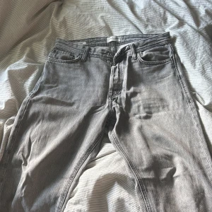 Grå jeans från Jack & Jones - Säljer ett par grå jeans från Jack & Jones med klassisk femficksdesign och normal passform. Jeansen har en snygg tvättad look och är tillverkade i ett mjukt denimtyg. Perfekta för dig som gillar stilrena och enkla jeans.
