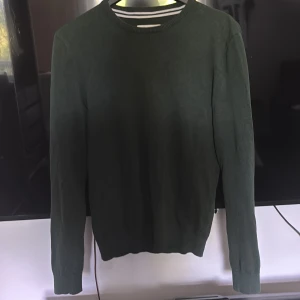Mörkgrön stickad tröja från Pier One - Mörkgrön stickad tröja från Pier One med rund halsringning och långa ärmar. Enkel och stilren design som passar perfekt till vardags. Ribbstickade muddar vid ärmslut och nederkant.