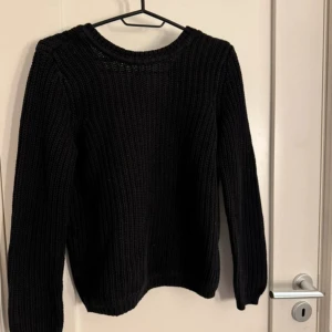 Svart stickad tröja med v-ringning och knyt - Säljer en svart stickad tröja med djup v-ringning och knyt i nacken. Tröjan har långa ärmar och ribbade muddar vid ärmslut och nederkant. Perfekt för lager-på-lager och enkel att styla till olika outfits.
