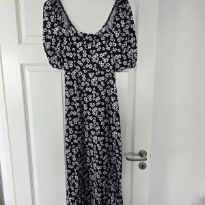 Svart blommig långklänning med puffärm - Säljer en svart långklänning med vita blommor och puffärmar. Klänningen har en djup rundad ringning och är tillverkad i ett mjukt, lätt material. Perfekt för sommarens alla tillfällen!