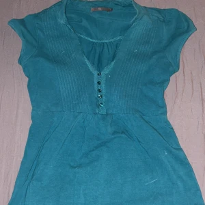 Turkos kortärmad blus från H&M - Turkos blus från H&M med v-ringning och dekorativa knappar framtill. Kortärmad modell med lätt rynk vid axlarna och sydda veck längs bysten. Perfekt för dig som gillar färg och enkel stil.💕💕