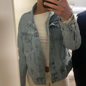 Ljusblå jeansjacka - Säljer en klassisk ljusblå jeansjacka med knappar framtill och bröstfickor. Jackan har en normal passform och är perfekt för vår och sommar. Enkel och stilren design som passar till många outfits.