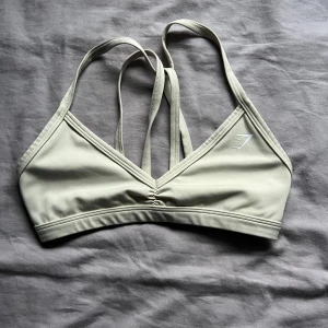 Beige sporttopp från Gymshark - Säljer en beige sporttopp från Gymshark med smala axelband och en stilren design. Perfekt för träning och ger bra stöd. Toppen har en diskret logga på framsidan och en bekväm passform.