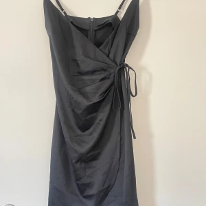 Svart omlottklänning - Elegant svart omlottklänning med knytning i midjan och dragkedja bak. Perfekt för en stilren look.