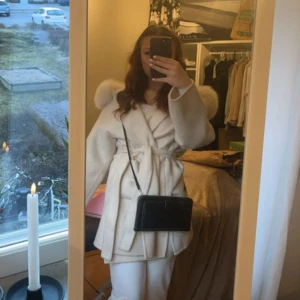Beige kappa med äkta päls - Säljer en elegant beige kappa med bälte och pälskrage. Perfekt för kyliga dagar med sin stilrena design och mjuka material. Kappan har långa ärmar och en klassisk passform. Vissa knappar på pälser har tyvärr ramlat men det är inget som inte går att sy!