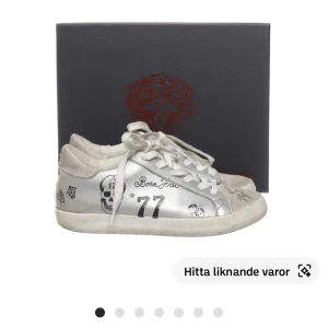 Silvriga sneakers från Ed Hardy - Snygga silvriga sneakers från Ed Hardy med coola tryck och snörning. Skorna har en rund tå och är dekorerade med unika mönster och motiv som ger en edgy look. Perfekta för dig som vill sticka ut med din stil.