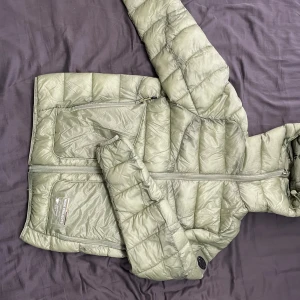 Grön dunjacka från Nude Project - Säljer en stilren grön vårjacka från Nude Project. Jackan har en praktisk dragkedja och en huva för extra skydd. Perfekt för kyligare dagar med sin quiltade design som håller värmen. Lätt och bekväm att bära. Pris går att diskutera vid snabb affär, ny pris är 1200kr och den är aldrig använd pga att den är för liten för mig