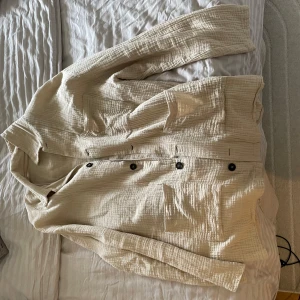 Beige overshirt från Zara - Säljer en stilren beige overshirt från Zara med långa ärmar och knappar framtill. Overshirten är tillverkad i ett lätt och luftigt material, perfekt för en avslappnad look. Passar bra till både jeans och chinos. Perfekt för vår och sommar!